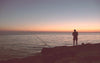 A man fishing off the rocks at sunset